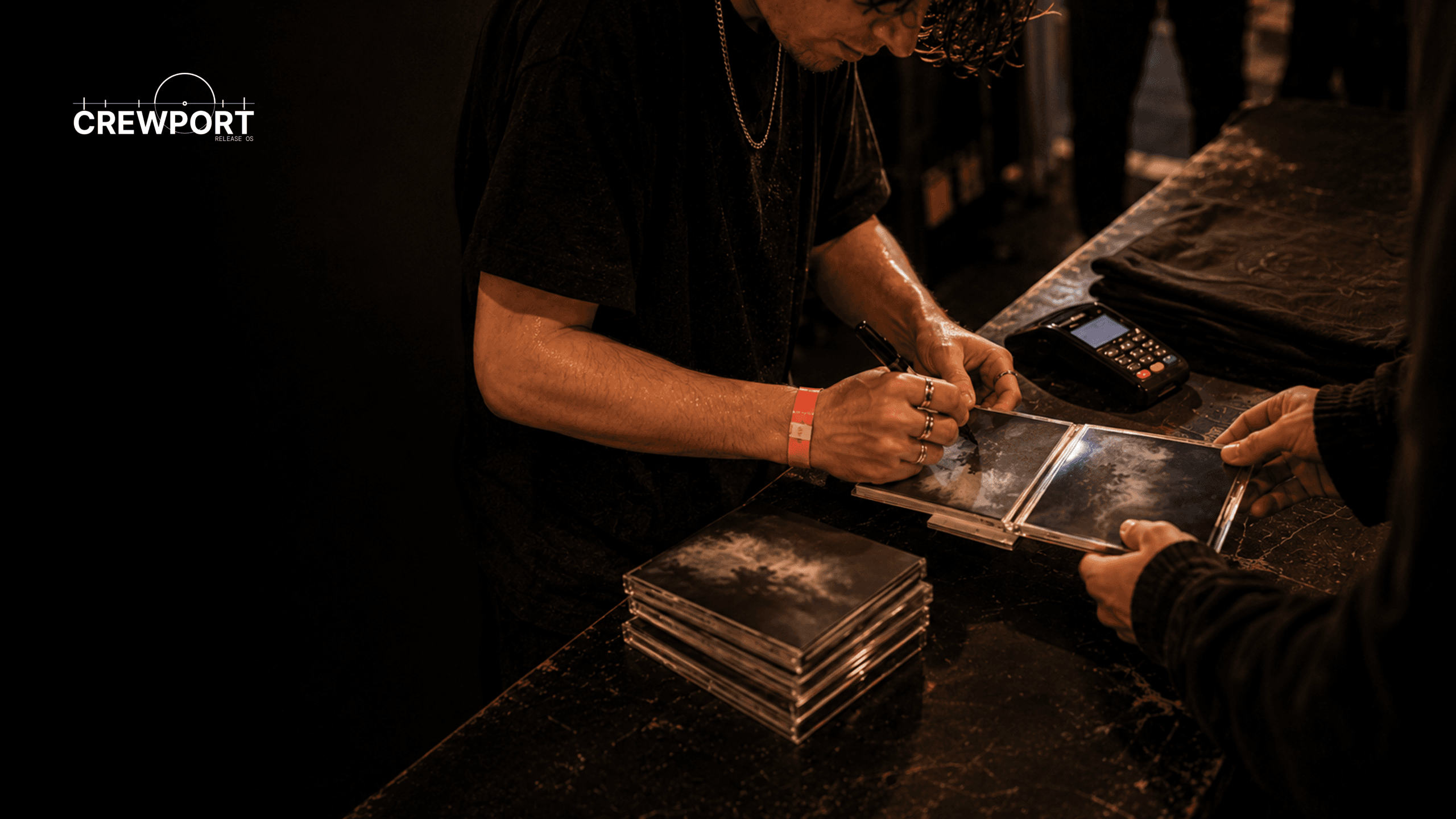 Independent artist signing a CD booklet for a fan at a small post-show merchandise table.